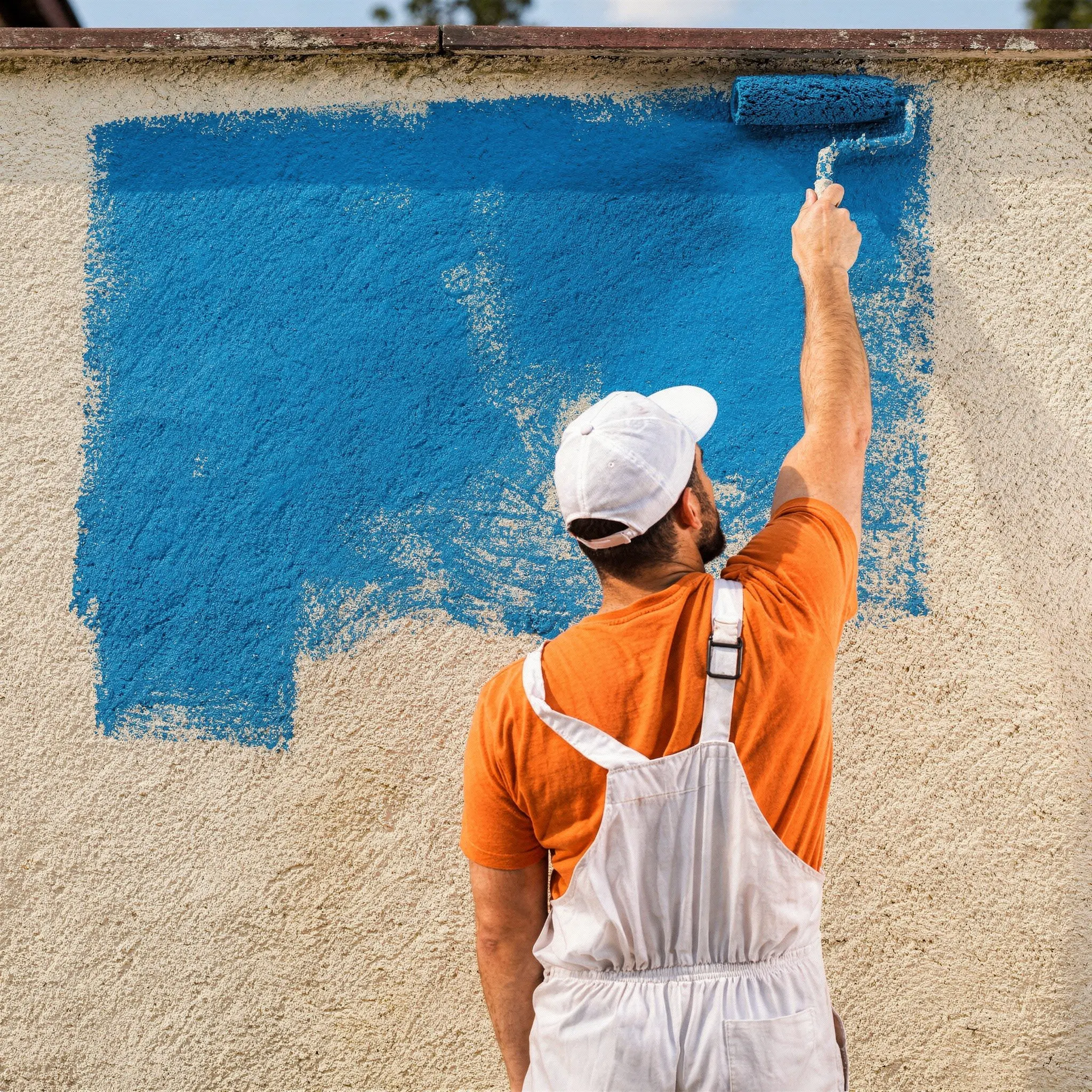 Artisan peintre appliquant de la peinture bleue au rouleau sur une façade extérieure de maison à Chalais en Charente