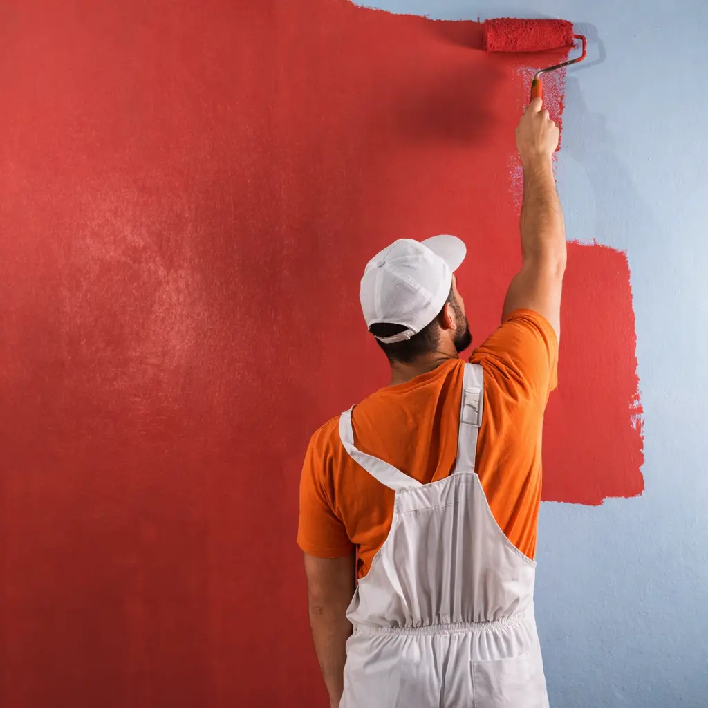 Artisan peintre appliquant de la peinture rouge au rouleau sur un mur intérieur avec finition uniforme à Chalais en Charente
